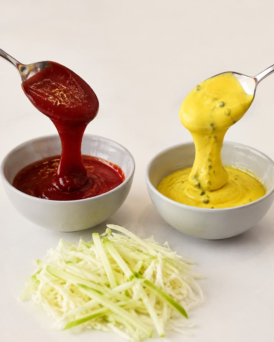 Rød karryketchup og gul agurkeremoulade kontrolleres i tykke bånd ved siden af tør æble-kål