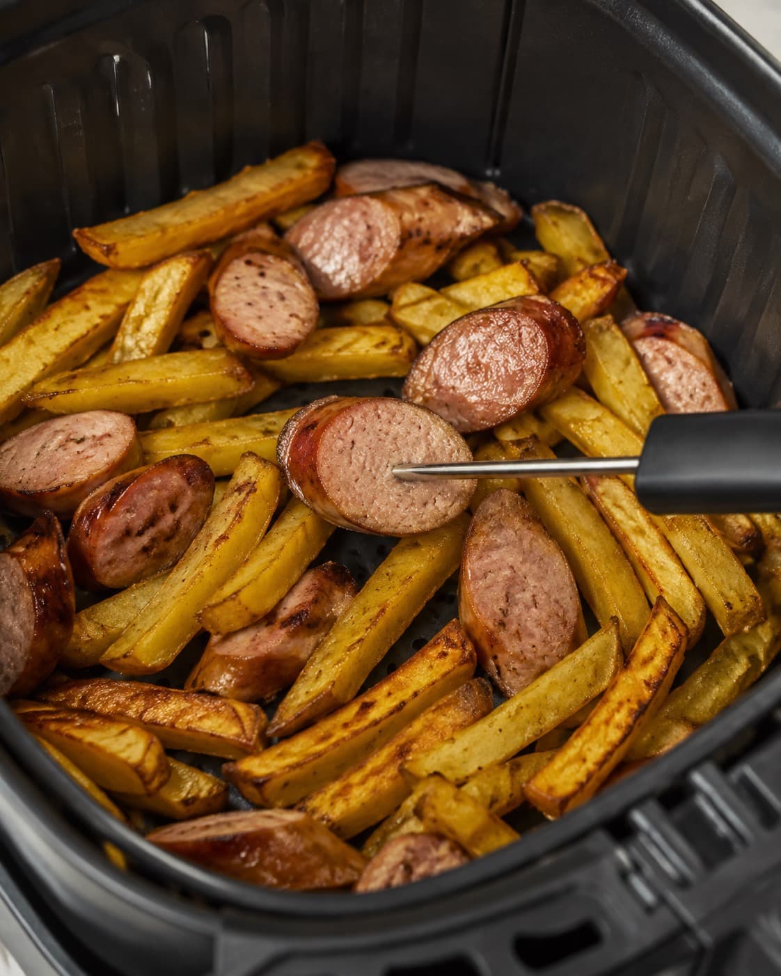 Pølseskive temperaturmåles blandt sprøde kartoffelstave i airfryer-kurven