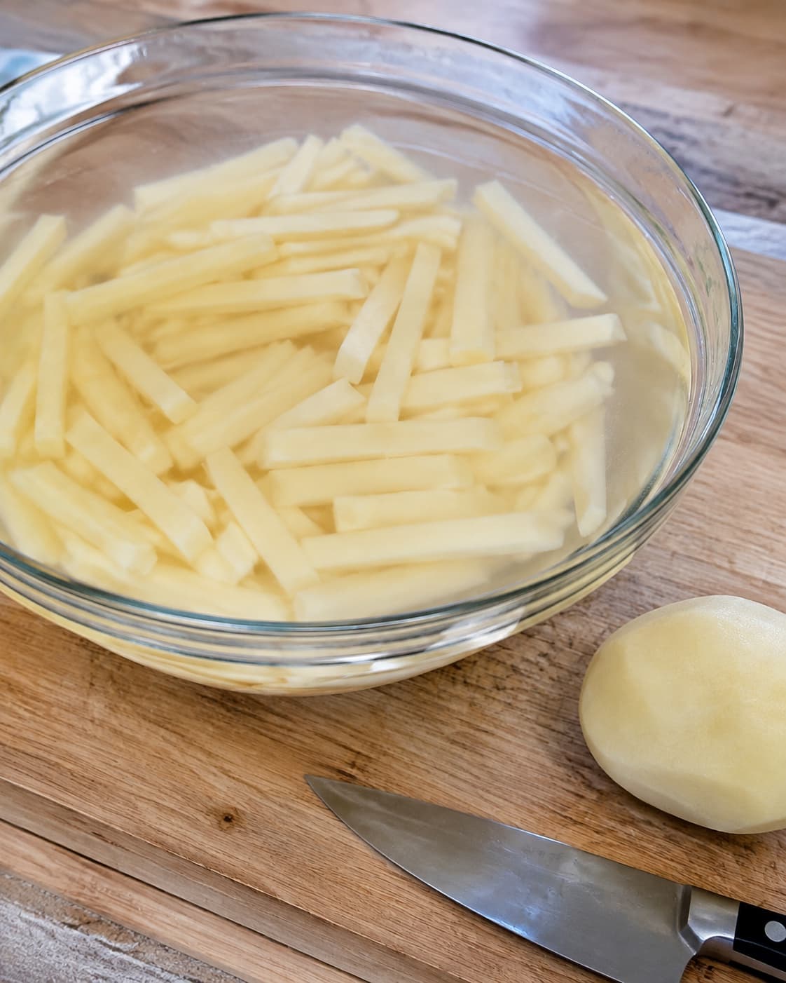 Ensartede rå kartoffelstave ligger nedsænket i iskoldt vand før airfryer-tilberedning