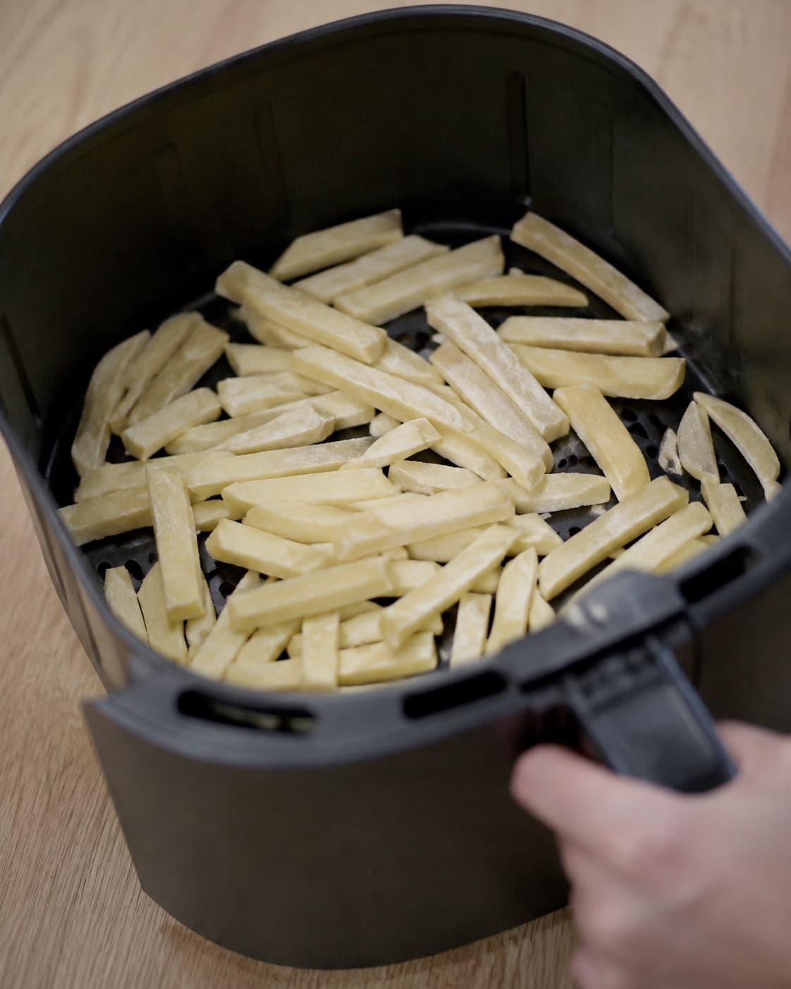 Blege halvtilberedte kartoffelstave ligger luftigt i airfryer-kurven efter første varmefase