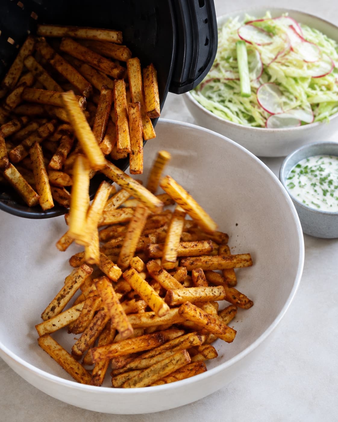 Lange gyldne pommes frites hældes fra airfryer og krydres før servering med dip og kålsalat