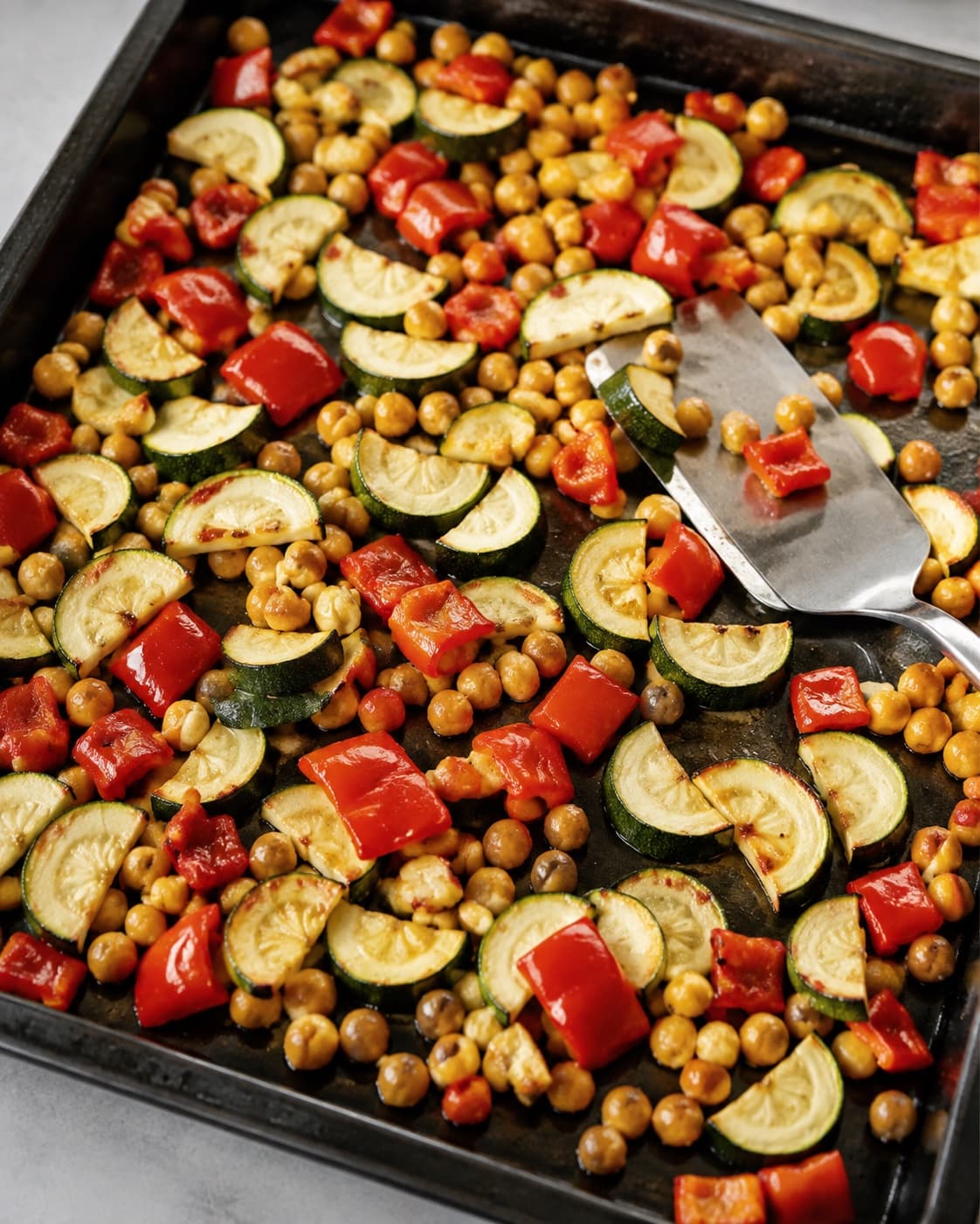 Kikærter, courgette og rød peberfrugt er ristede lysegyldne på en stor bageplade