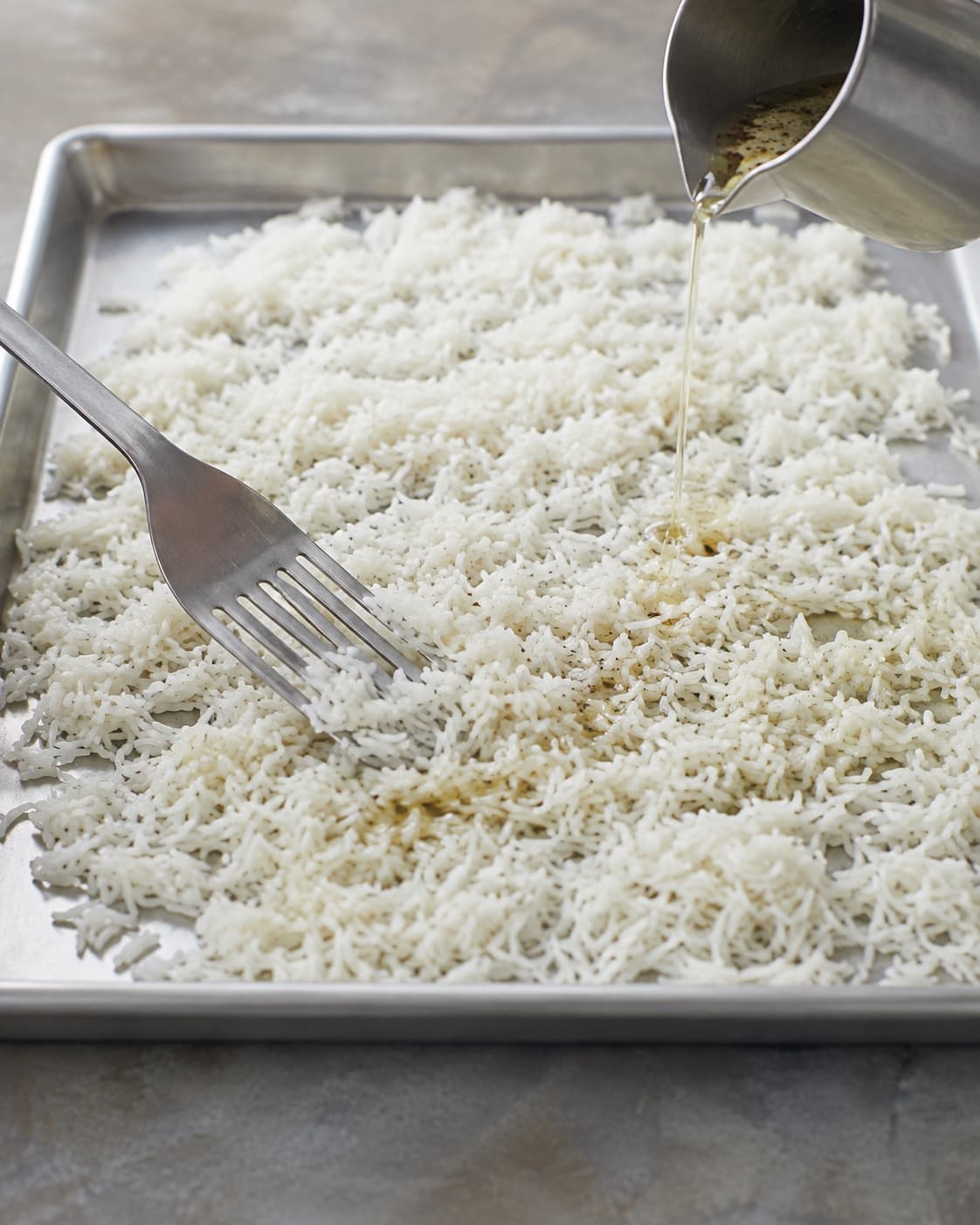Nykogte basmatiris ligger i et højst 2 cm lag på metalbakke og vendes med citron-sumakvinaigrette