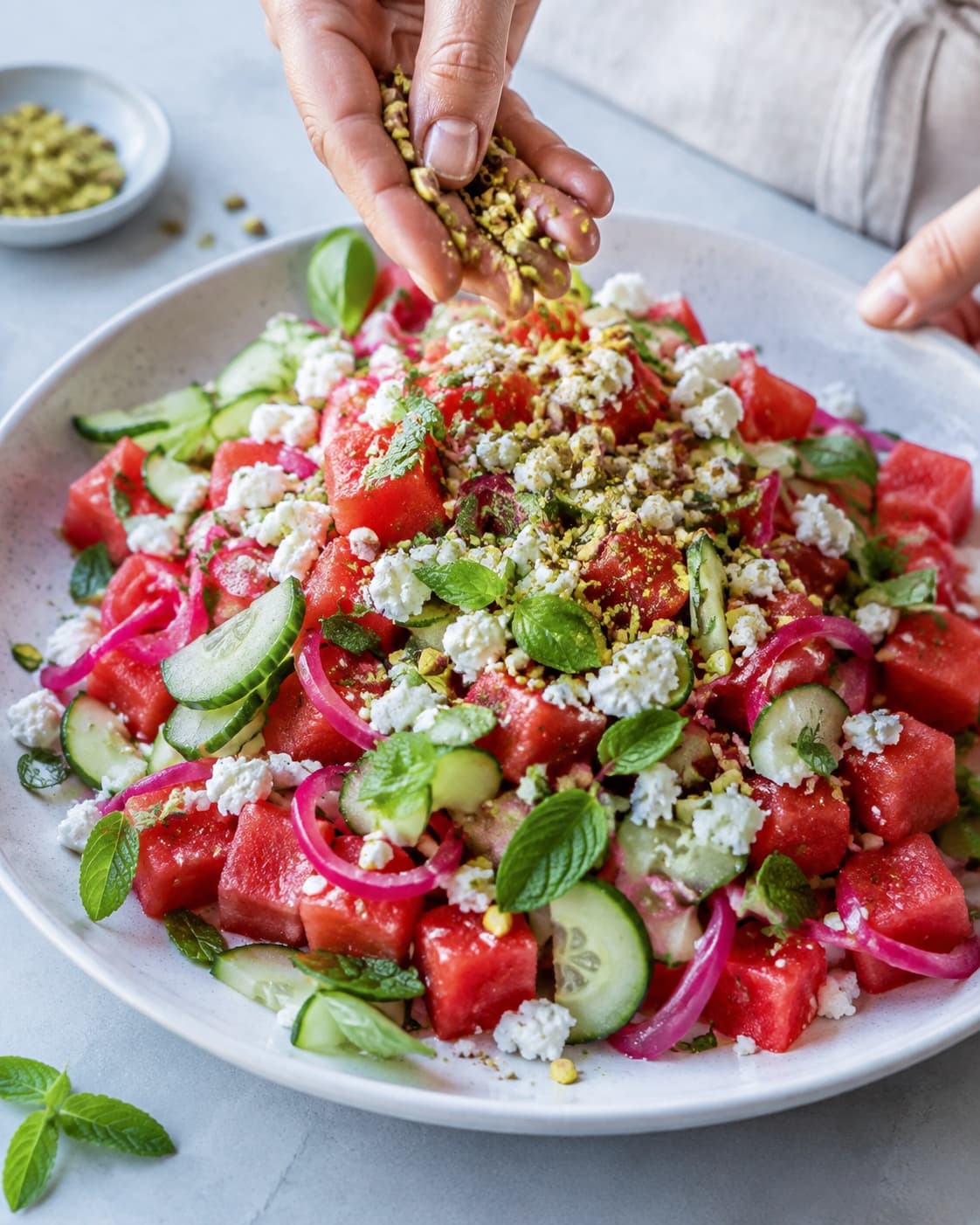 Vandmelon og agurk foldes nænsomt med feta, pink løg, urter og pistacie på et fad