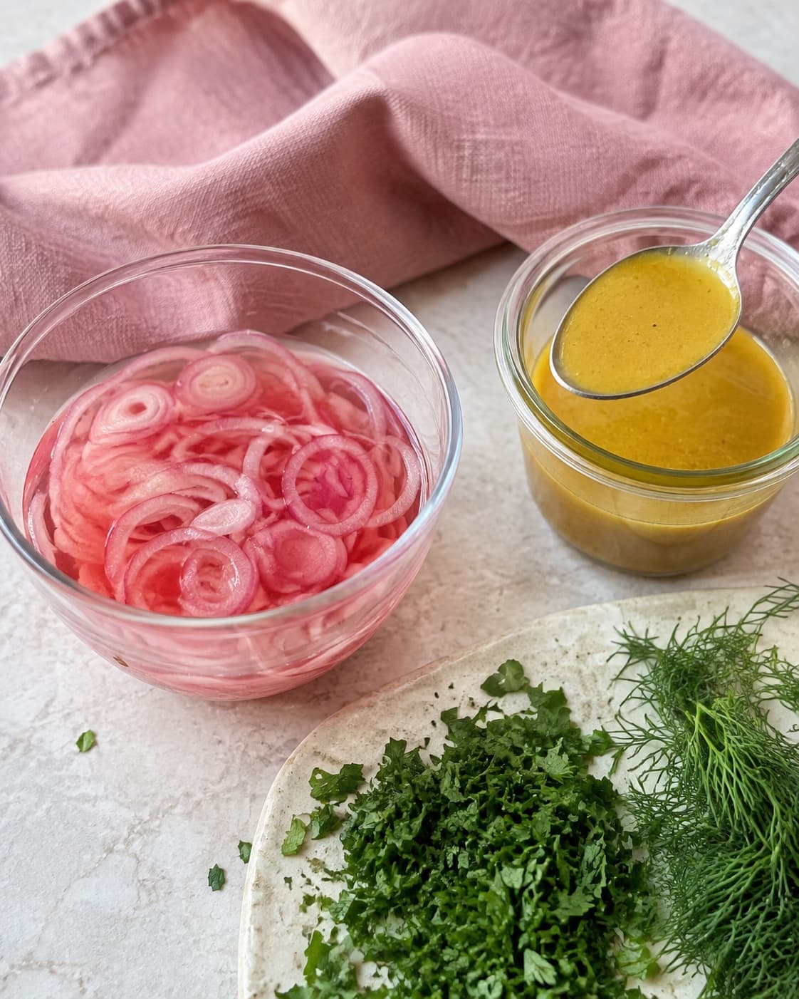Lyserøde syltede skalotteløg står ved en blank gylden sennepsvinaigrette