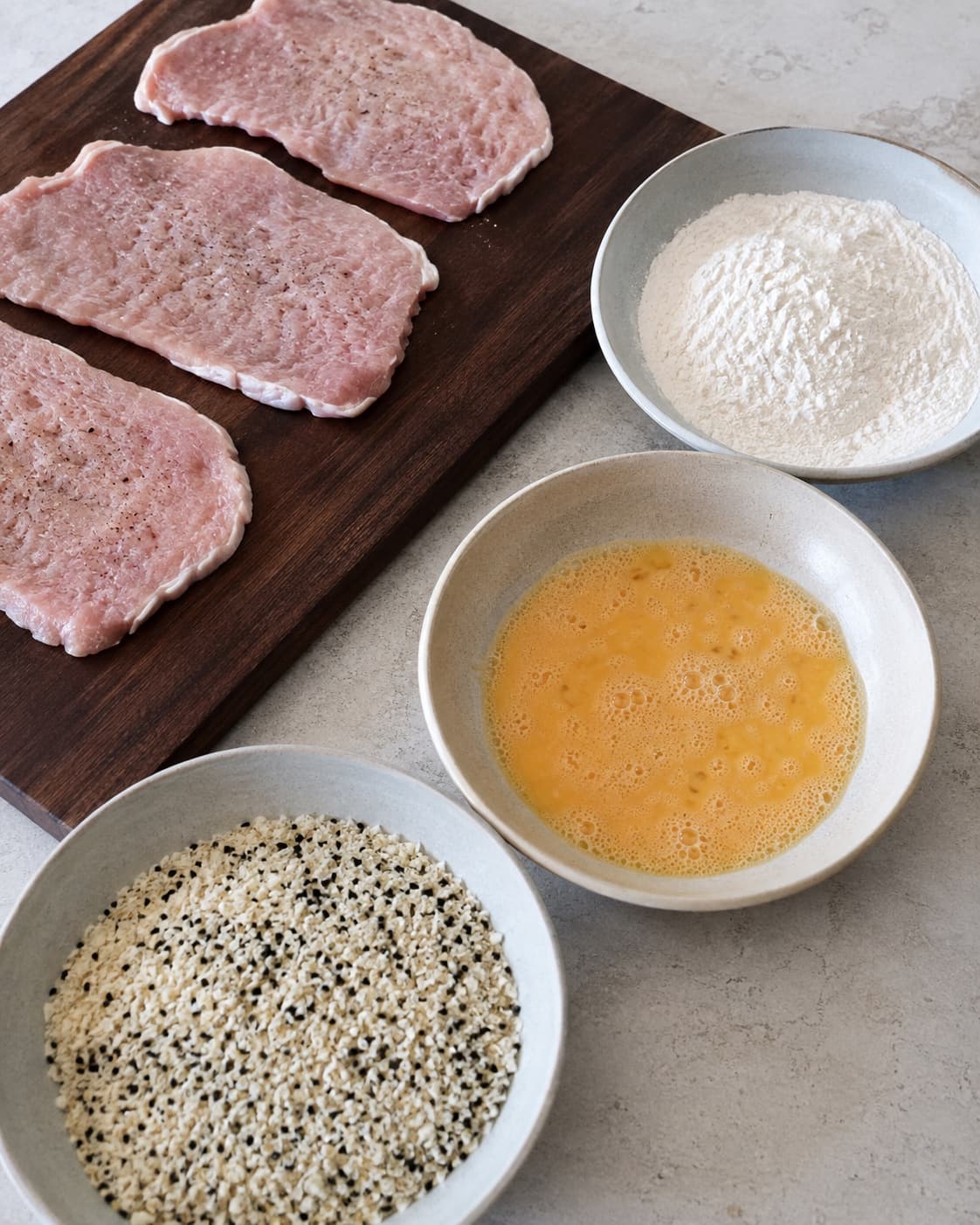 Tørrede jævne koteletter står ved tre adskilte fade med mel, æg og panko-sesam