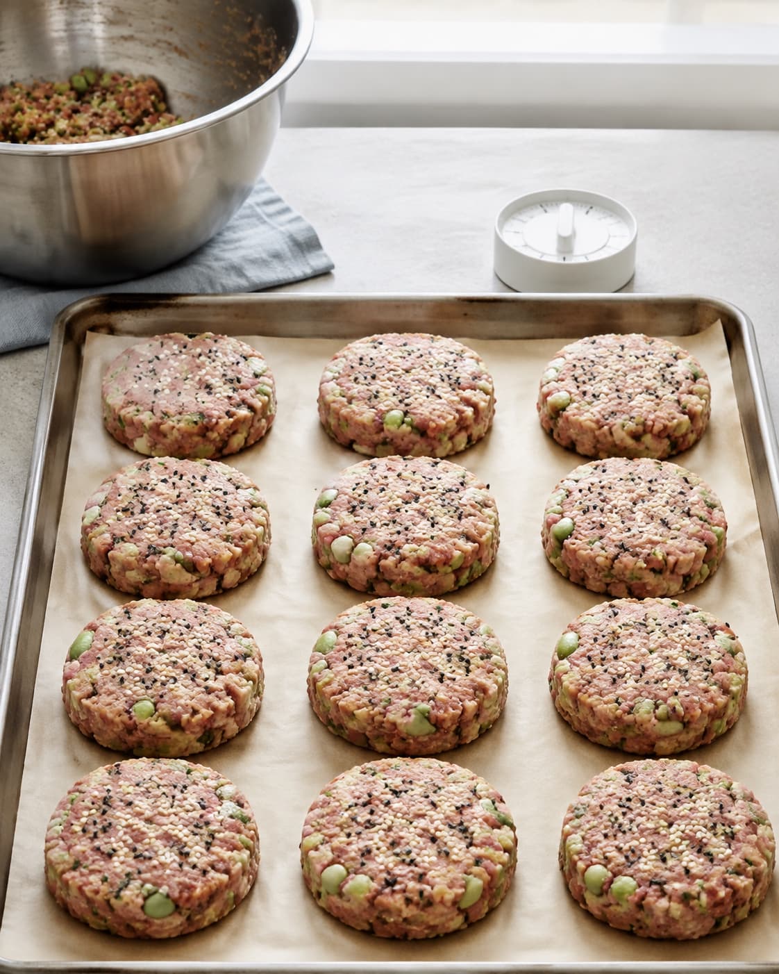 Tolv kolde tun-edamamefrikadeller formes og dækkes let med sesam