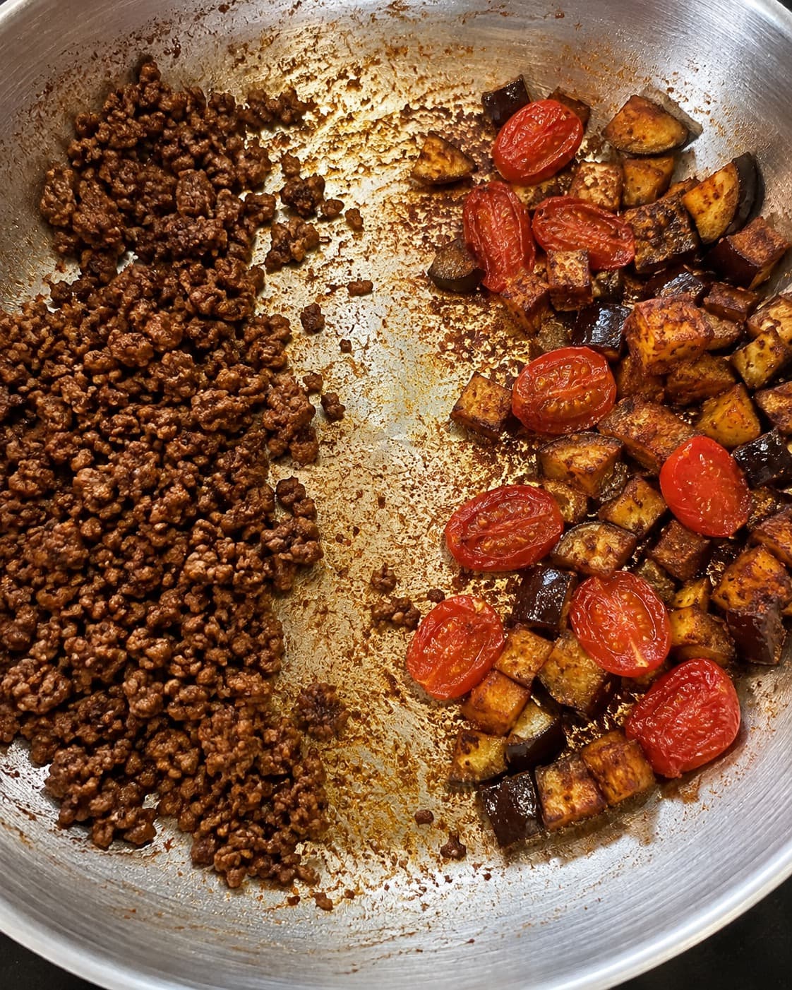Gennemstegt smuldret oksekød og gyldne auberginetern med tomater brunes tørt i hver sin side af panden