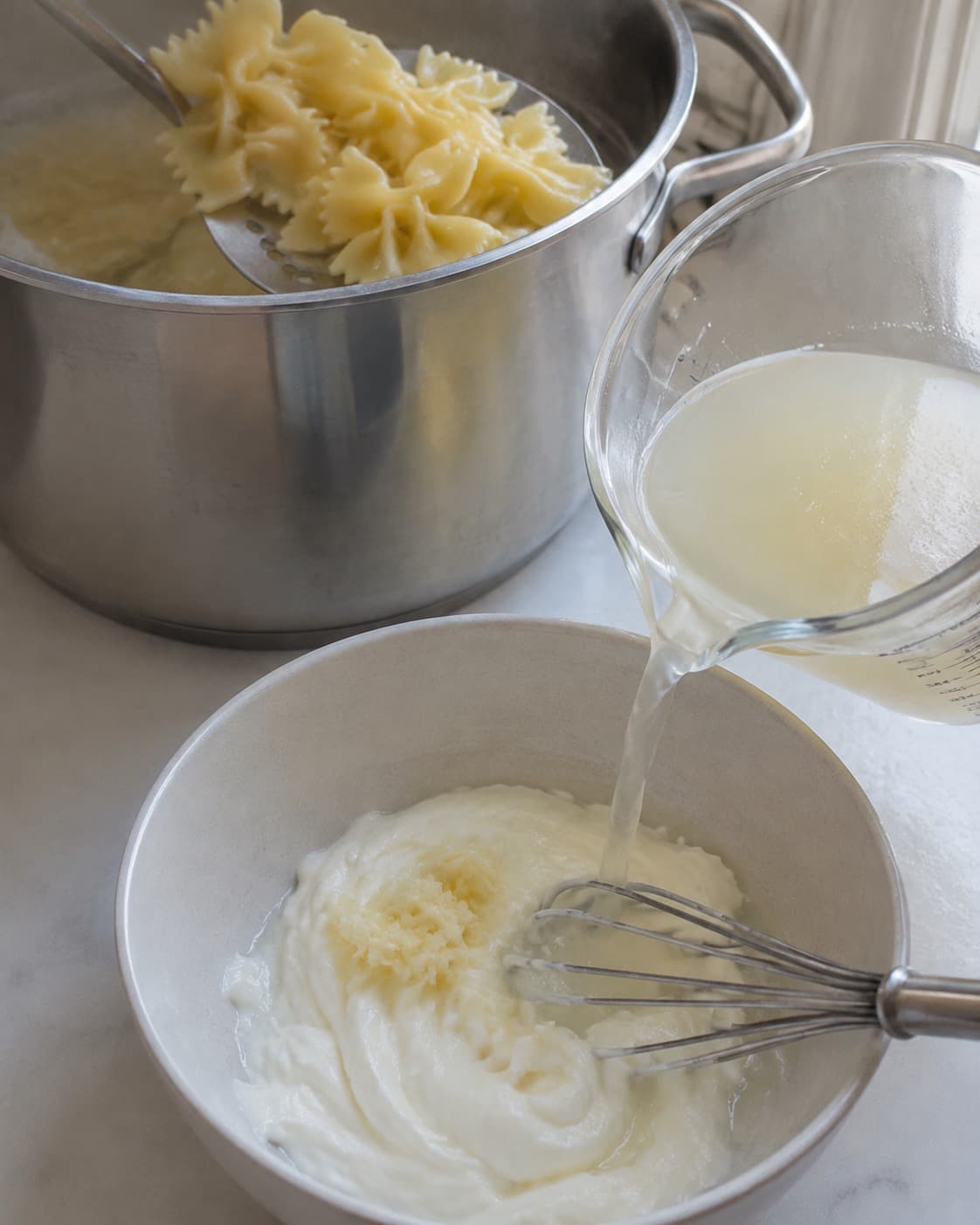 Farfalle løftes al dente, pastavand måles, og en lille lun mængde piskes i hvidløgsyoghurt